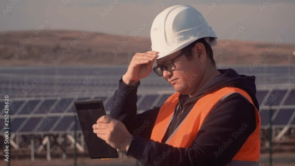 engineer of Asian appearance is carefully studying the report on work on the tablet and adjusts his helmet on his head engineer of Asian appearance is carefully studying the report on work on the tablet and adjusts his helmet on his head