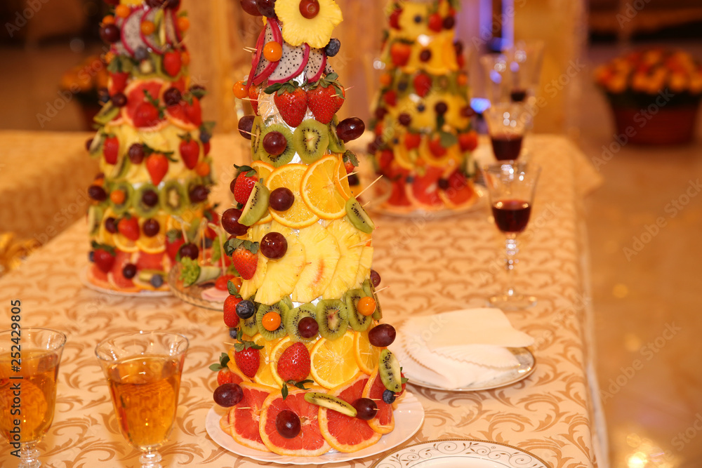 festive pyramid of fresh fruits and berries on a table with red wine and champagne