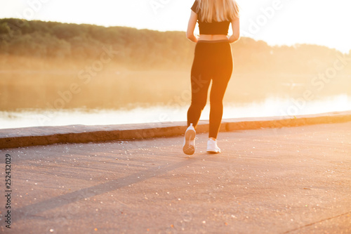 A woman with a slim, muscular figure runs around in black sports clothes and white sneakers in nature.