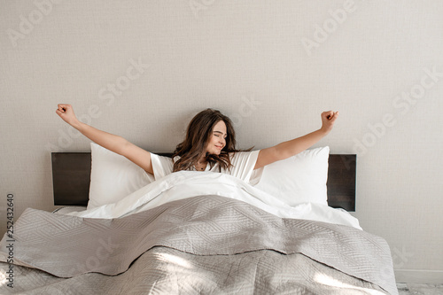 Young woman in the bed. Smiling beautiful woman in pajamas is waking up, good morning in the bedroom
