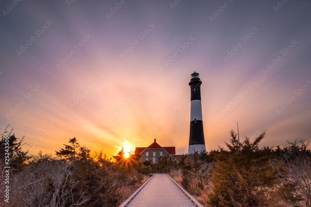 Boardwalk path leading to lighthouse. Vibrant colorful sunset as clouds streak across the sky. Fire Island New York