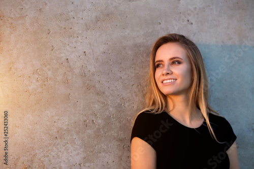 Horizontal portrait of beautiful smiling blonde woman on outdoor wall background with copyspace.