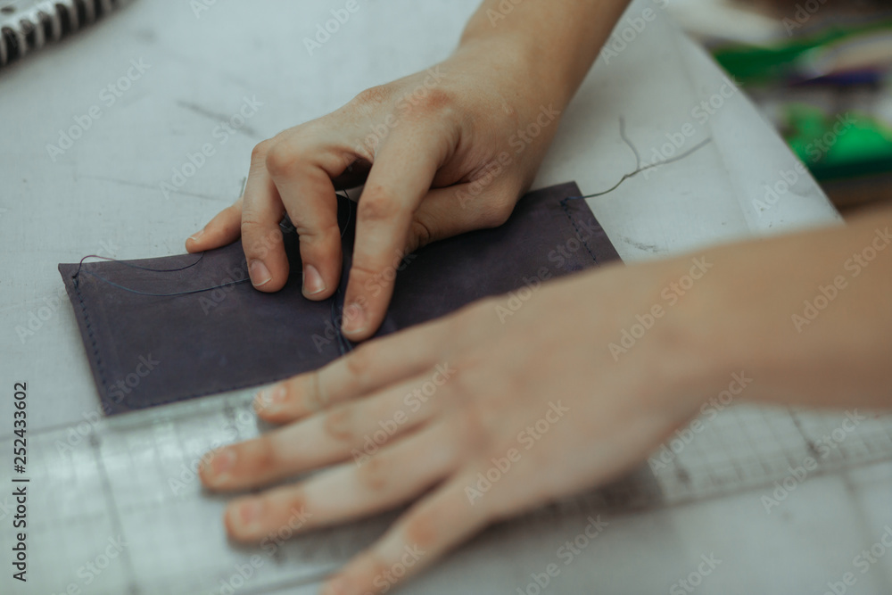 Handmade leather artisan making craft wallet using piece of natural leather on his working place with tools, close up photo of his hands Handmade leather artisan making craft wallet using piece of natural leather on his working place with tools, close up photo of his hands