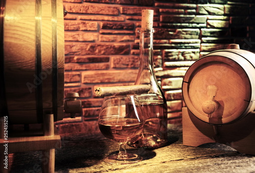 Glass of cognac and whiskey in the barrel background.Cigar.Luxury lifestyle.Wine cellar.Quality alcohol.Stone wall.Retro & Vintage style. © erkipauk