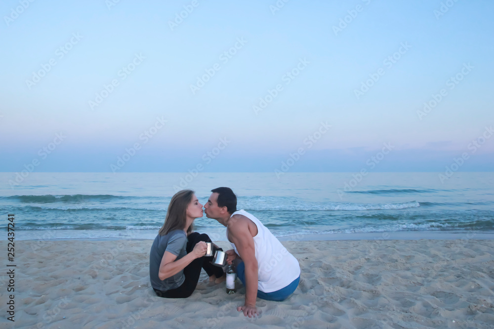 Woman and man are sitting on the sea beach and meeting sunset and kissing