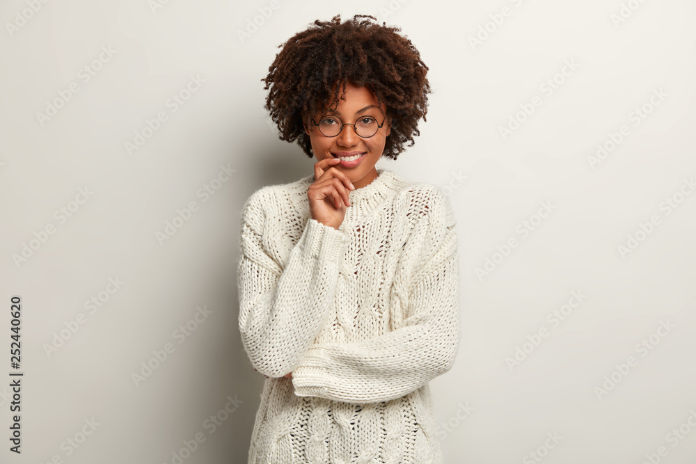 Gentle cheerful woman with satisfied facial expression, wears oversized sweater, rejoices good news, isolated over white background. Optimistic African American girl enjoys life. Emotions concept Gentle cheerful woman with satisfied facial expression, wears oversized sweater, rejoices good news, isolated over white background. Optimistic African American girl enjoys life. Emotions concept