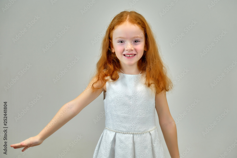 Fototapeta premium Concept portrait of a cute pretty child girl with red hair on a gray background smiling and talking