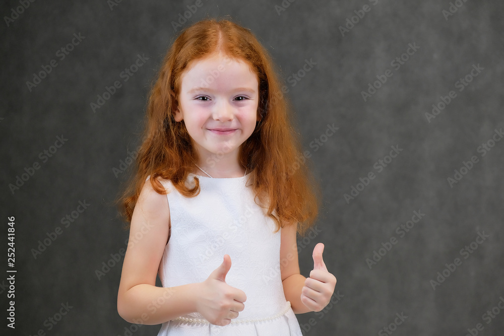 Concept portrait of a cute pretty child girl with red hair on a gray background smiling and talking