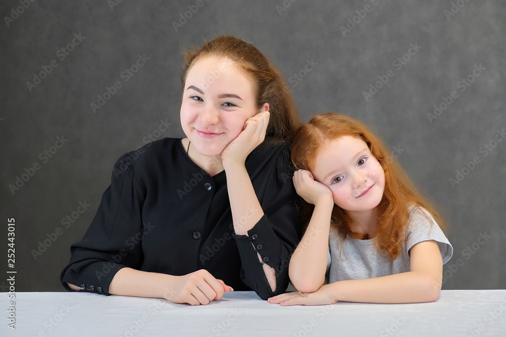 Concept portrait of two cute pretty girls sisters with red hair on a gray background smiling and talking. Concept portrait of two cute pretty girls sisters with red hair on a gray background smiling and talking.
