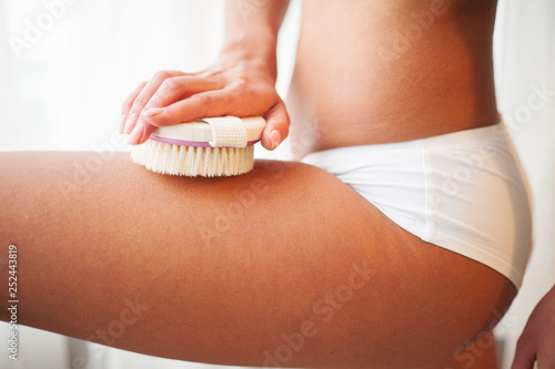 Woman's arm holding dry brush to top of her leg. Cellulite treatment, dry brushing
