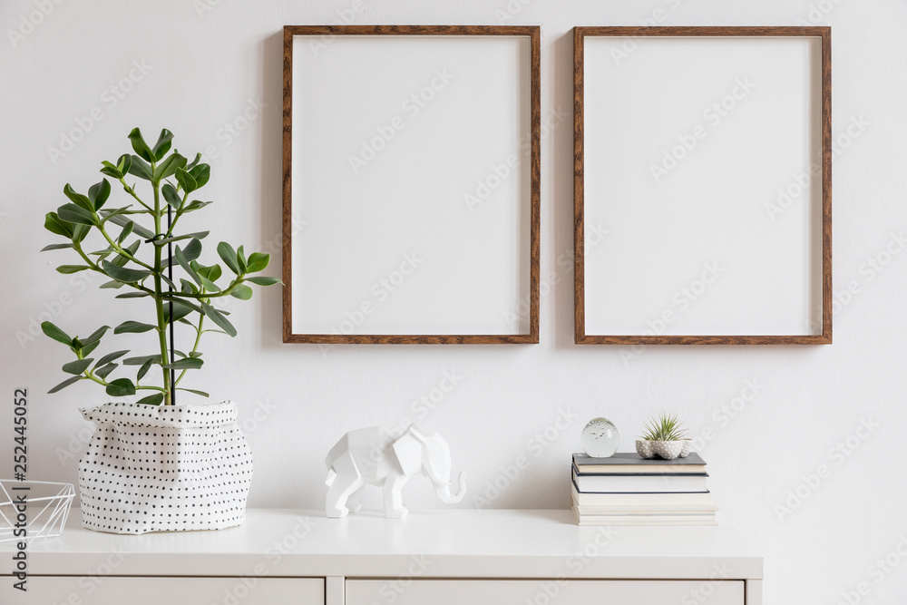 Fototapeta Stylowy biały wystrój wnętrza z dwiema brązowymi drewnianymi ramkami na zdjęcia z książkami, piękną rośliną w stylowej doniczce, figurką słonia i akcesoriami do domu. Minimalistyczny skandynawski pokój.