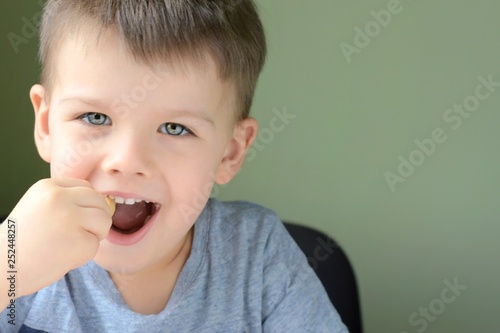 Emotional portrait of a white handsome caucasian blue eyed boy on neural blurred background. Smiling cute toddler boy eating candy.  photo