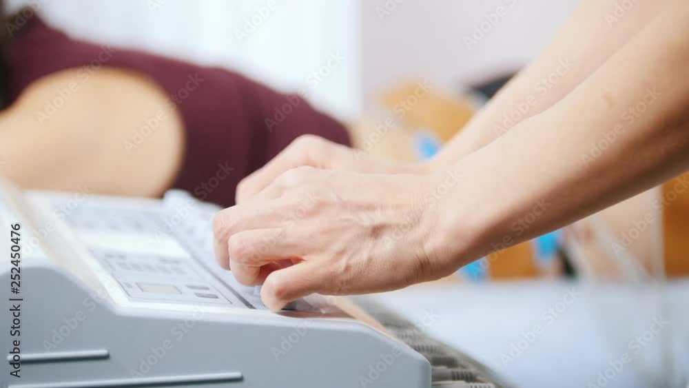 Cosmetology clinic. Young woman taking myostimulation, lying in bed. A doctor turns on the machine for myostimulation Cosmetology clinic. Young woman taking myostimulation, lying in bed. A doctor turns on the machine for myostimulation