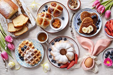 Easter festive dessert table with hot cross buns, cakes, waffles and pancakes. Overhead view
