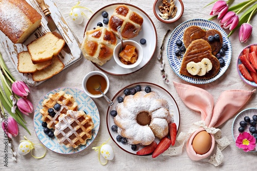 Easter festive dessert table with hot cross buns, cakes, waffles and pancakes. Overhead view