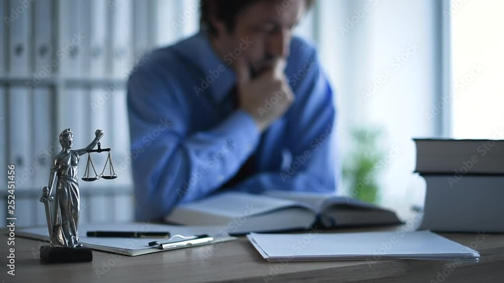 Attorney reading book in law office, selective focus on statue of Lady Justice Attorney reading book in law office, selective focus on statue of Lady Justice