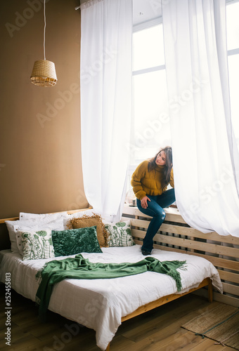 Young woman sitting on sill near big window in bedroom