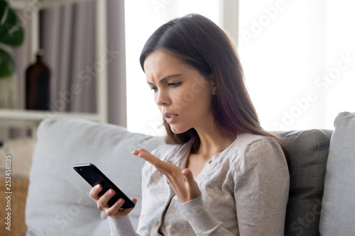 Upset young woman having problem with mobile phone, reading bad news