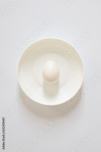one fresh white egg lies on a white plate on a light background. Copy space for lettering and design