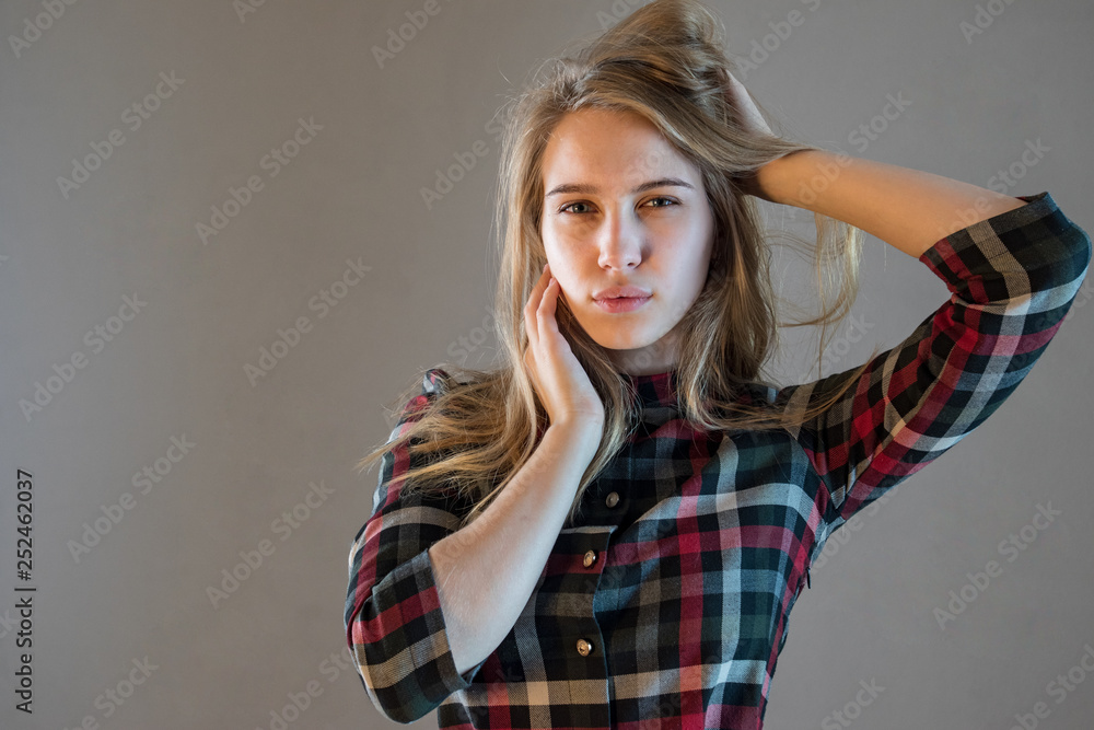Fototapeta premium young blonde girl in plaid dress touches her hair. woman poses for camera demonstrating natural beauty without cosmetic and makeup. Tender emotions and coquetry