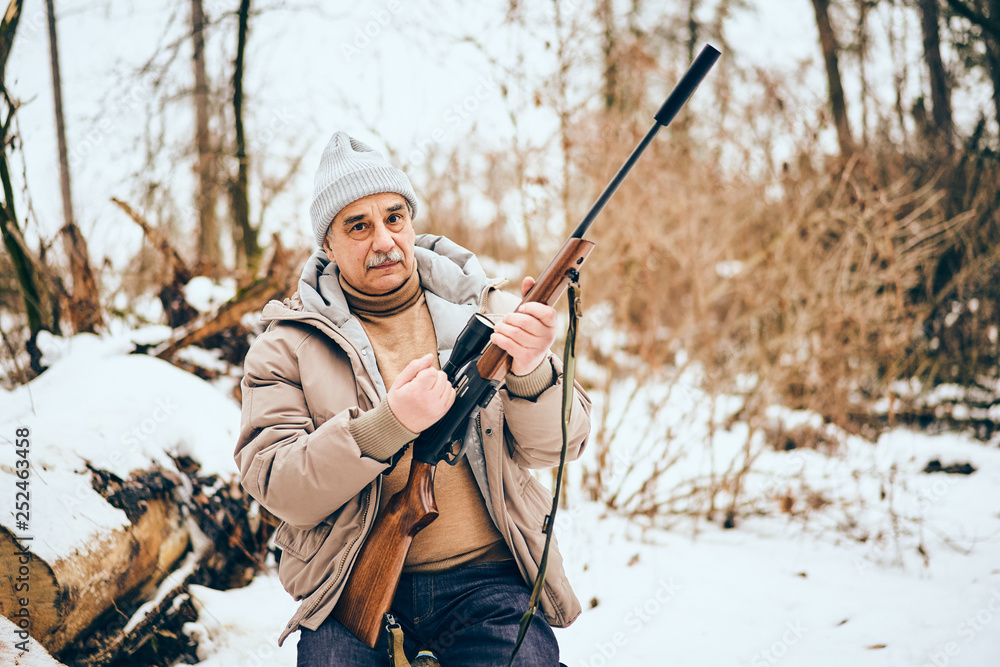 Fototapeta premium Senior man sitting in a personal lumber yard with a rifle