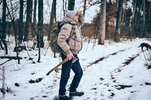 Senior man wearing stylish winter clothes and backpack traveling in a forest