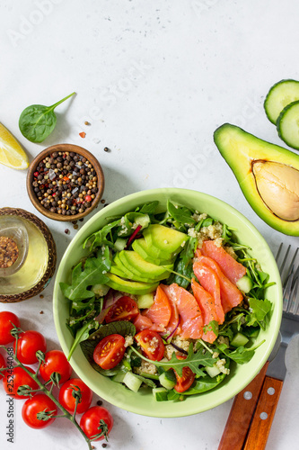 Diet menu concept. Summer Healthy salad with quinoa, Tomatoes, Salmon, Avocado and arugula. Top view flat lay background on light stone table with copy space.
