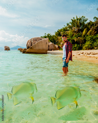 young men on tropical beach with palm tree, white beach man walking Seychelles Island, tanning men on tropical vacation photo