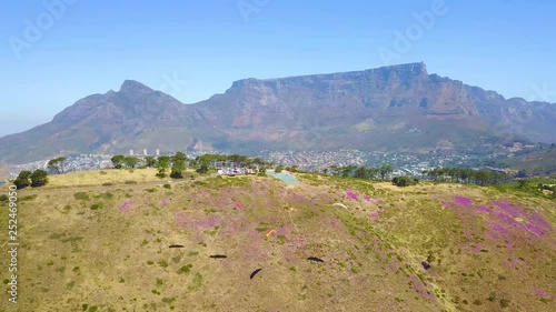 Drone aerial over paragliding and paragliders with Table Mountain Cape Town, South Africa, in background.