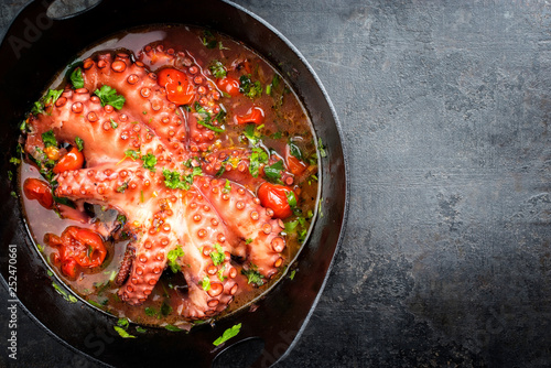 Traditional Greek octopus braised cooked with tomatoes and herbs in ouzo sauce as top view in a cast-iron saucepan with copy space right
