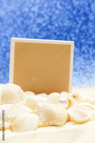 Blank paper and seashells on white and beach against blurred bokeh blue background, travel concept template