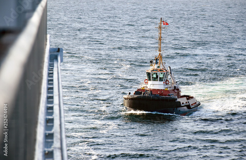 A tugboat navigates on the sea to assista cruise ship entering the port