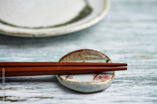 Empty ceramics plate, wooden chopsticks and chopstick rest on rustic wooden background. Close up. Copy space. 