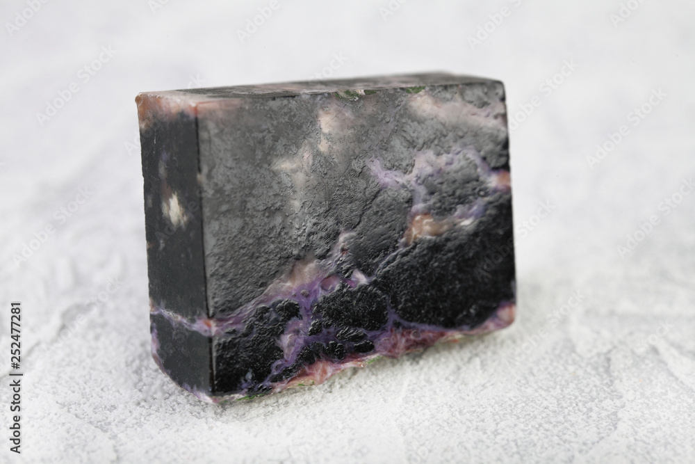 Natural mineral stone - polished charoite gemstone on white cement background. Natural mineral stone - polished charoite gemstone on white cement background.