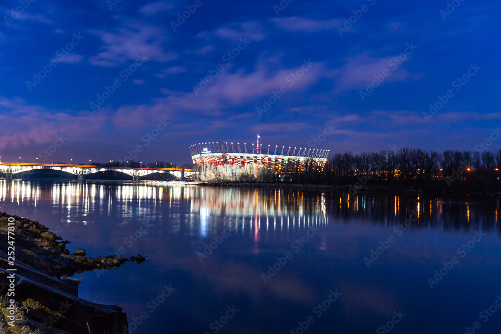 WARSAW, POLAND - FEBRUARY 14, 2019: National Stadium in Warsaw. Night and water reflections in  Vistula River.