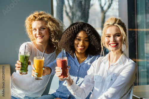 Portrait of three female multi etnic friends at a cafe drinking healthy frozen beverages. Multi-racial and difference of cultures friendship concept.