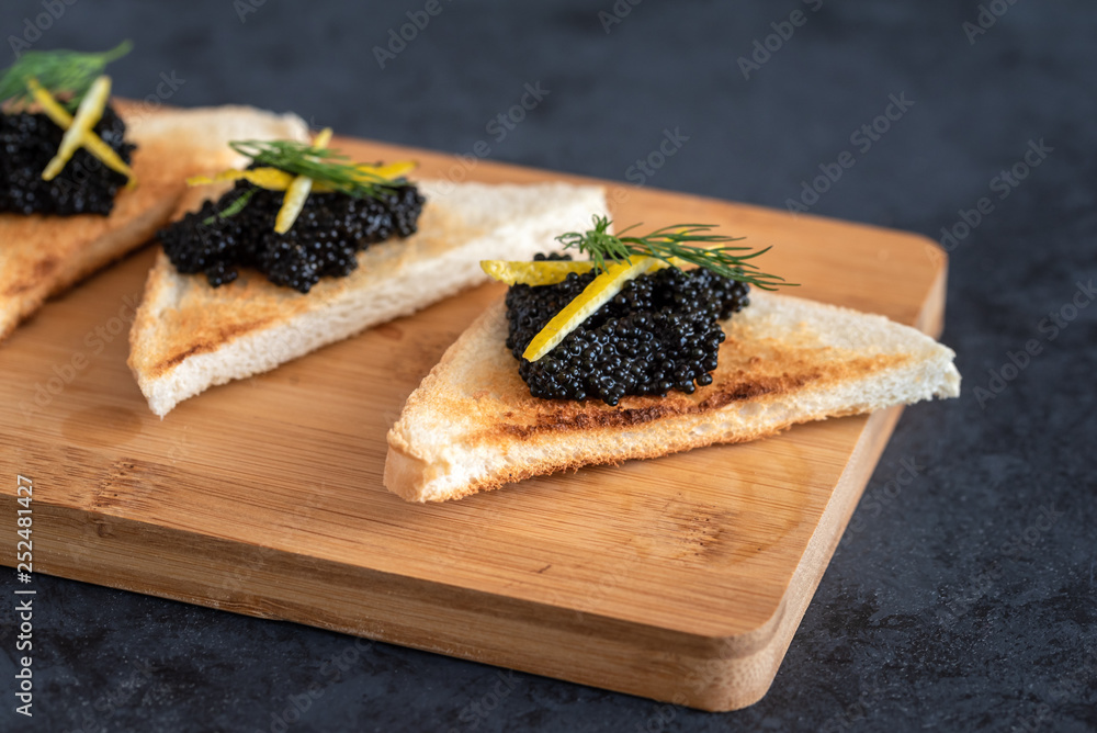 Appetizer toast bread with black caviar decorated by lemon pill and dill Appetizer toast bread with black caviar decorated by lemon pill and dill