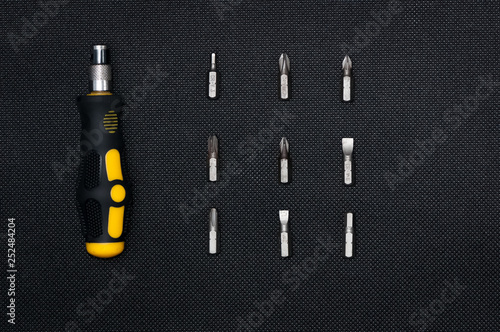 Black and yellow interchangable screwdriver with different bits surrounding. On dark dark background. photo