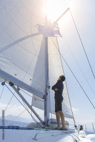 Photo A man on a sailing yacht stands with his back and looks at the open sails