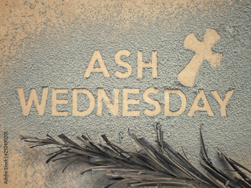 Ash Wednesday concept - Ash Wednesday words and a cross formed out of ashes. There’s a dry palm leaf under them.