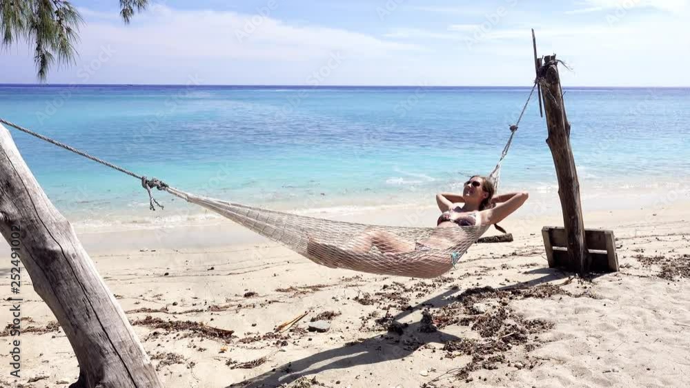 4K HOLIDAYS Young caucasian woman in bikinis relaxing in a hammock on a white sand beach. Woman lying in hammock on beautiful exotic beach on remote Gili islands, Bali 4K HOLIDAYS Young caucasian woman in bikinis relaxing in a hammock on a white sand beach. Woman lying in hammock on beautiful exotic beach on remote Gili islands, Bali