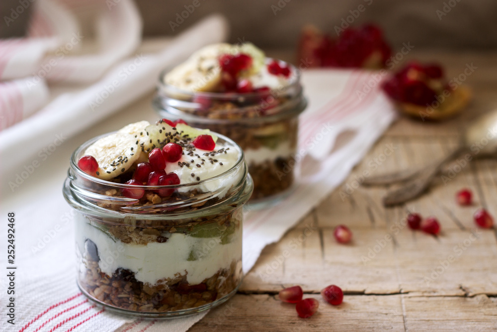 Granola with yogurt and fruit in glass jars on a wooden table. Rustic style. Granola with yogurt and fruit in glass jars on a wooden table. Rustic style.