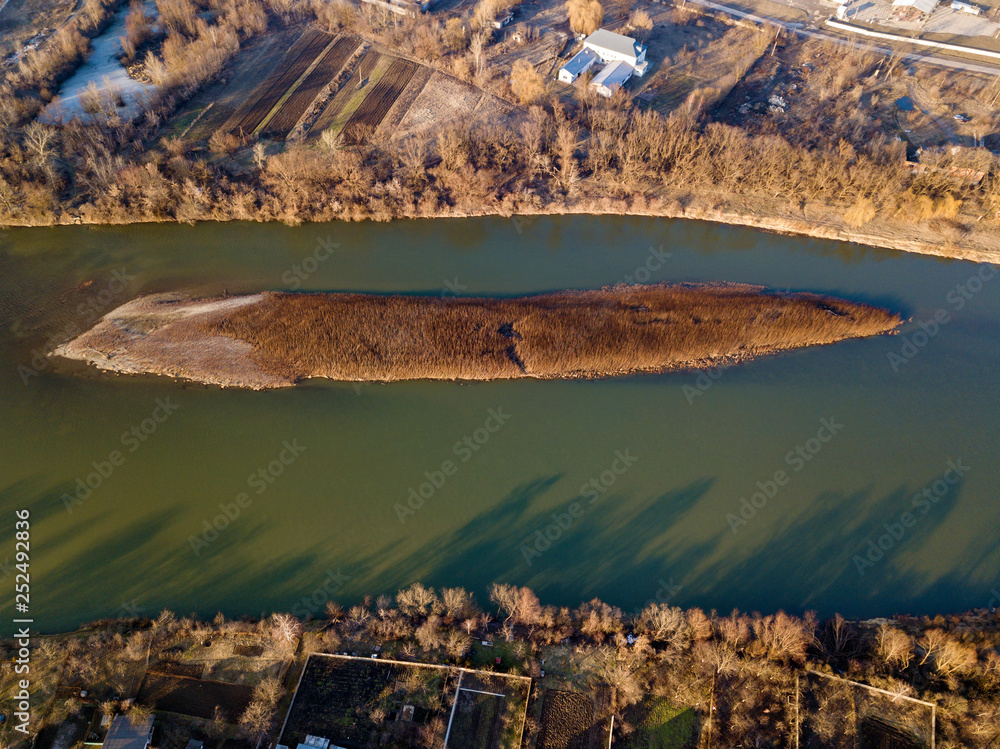 Aerial top view, countryside panorama of small island with dry grass in quiet river on sunny day. Drone photography.