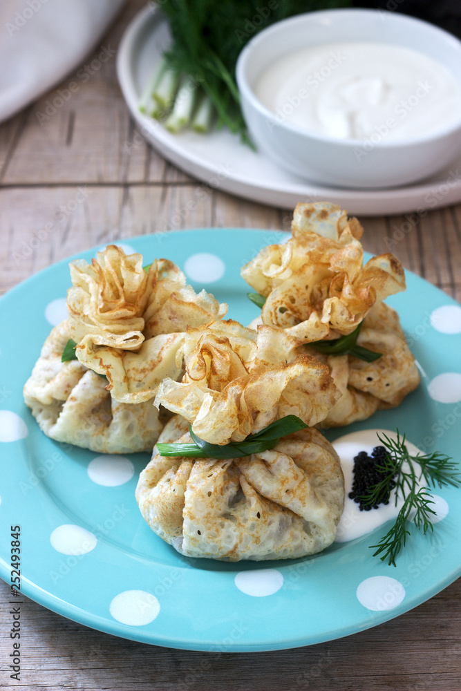 Bags of pancakes stuffed with herring, served with caviar, sour cream and dill on a wooden background. Rustic style. Bags of pancakes stuffed with herring, served with caviar, sour cream and dill on a wooden background. Rustic style.