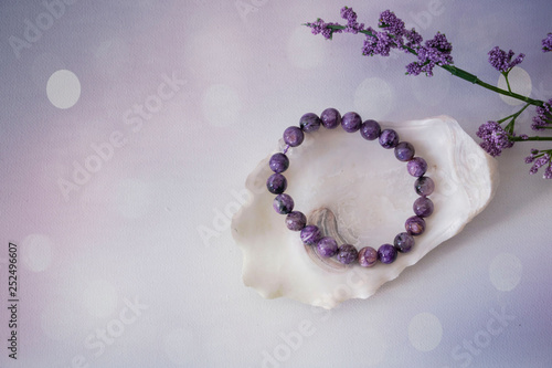 An close-up of an amethyst bracelet on a seashell next to a purple flower with a purple and white bokeh background Fototapeta