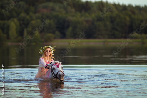 Blonde girl in white and red bodypain bathes with a horse in the lake at sunset. photo