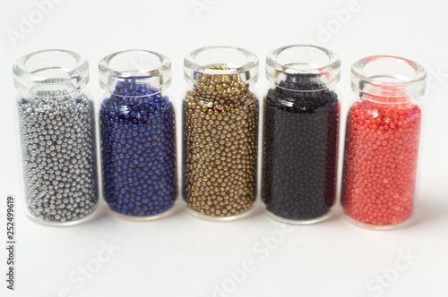 Multicolored beads in glass jars. Beads are poured on a white background. Plastic multi-colored polymers. Plastic pillets.