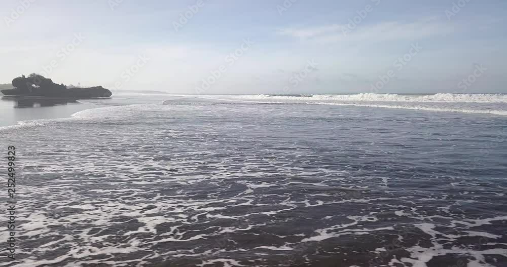 Aerial drone view beach with dark black sand. Sporty woman walk by the beach with white surf board surfing. Aerial view of the tropical beach. Pantai Yeh Gangga beach at Bali. Aerial drone view beach with dark black sand. Sporty woman walk by the beach with white surf board surfing. Aerial view of the tropical beach. Pantai Yeh Gangga beach at Bali.
