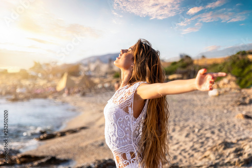 Junge, blonde Frau streckt ihre Arme am Strand aus und genießt die Freiheit und Ruhe photo