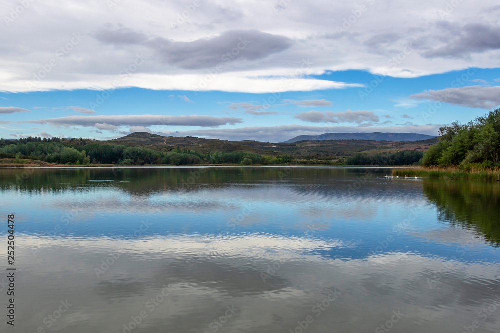 Overcast sky reflections on Pantano de la Grajera or La Grajera Reservoir surface on the Way of St. James, Camino de Santiago near Logrono, La Rioja, Spain Overcast sky reflections on Pantano de la Grajera or La Grajera Reservoir surface on the Way of St. James, Camino de Santiago near Logrono, La Rioja, Spain